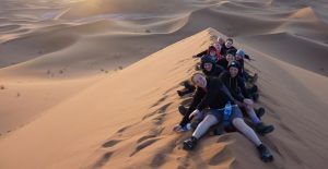 A group of people sitting on a dune on the Sahara Desert.