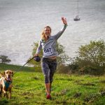 A person waving and running with a dog on a lead