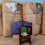Books wrapped in brown paper with a frog ornament sitting on a chair. Blind date with books.
