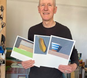 Artist Philip Lyons holding up his 3 pieces of donated art work.