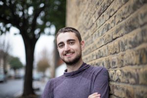 Person standing by a wall outside smiling.
