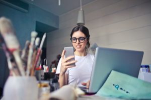 Person smiling as they look at their mobile phone as they sit at a desk with a computer
