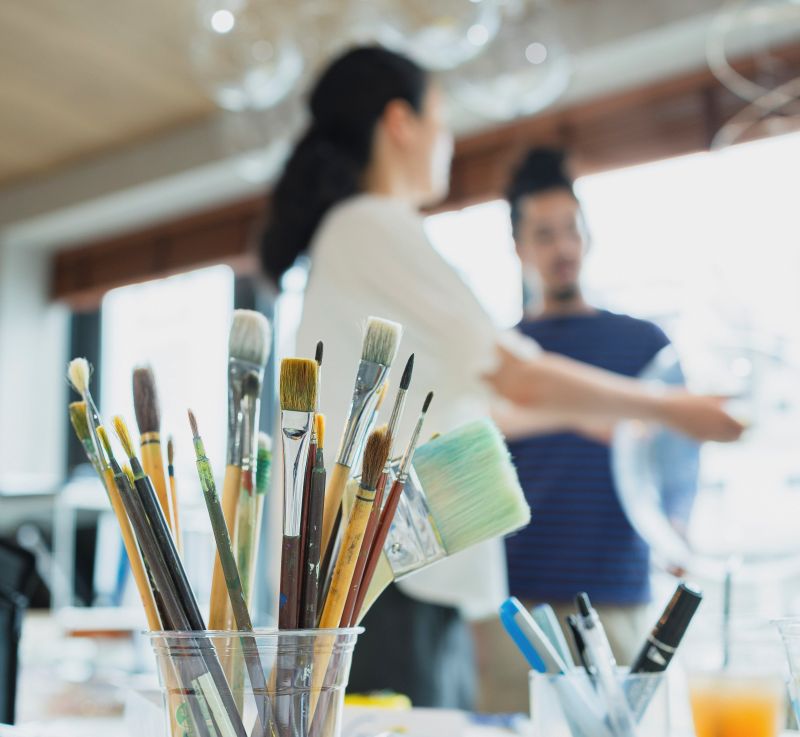 Two people in the background with a pot of paintbrushes in front